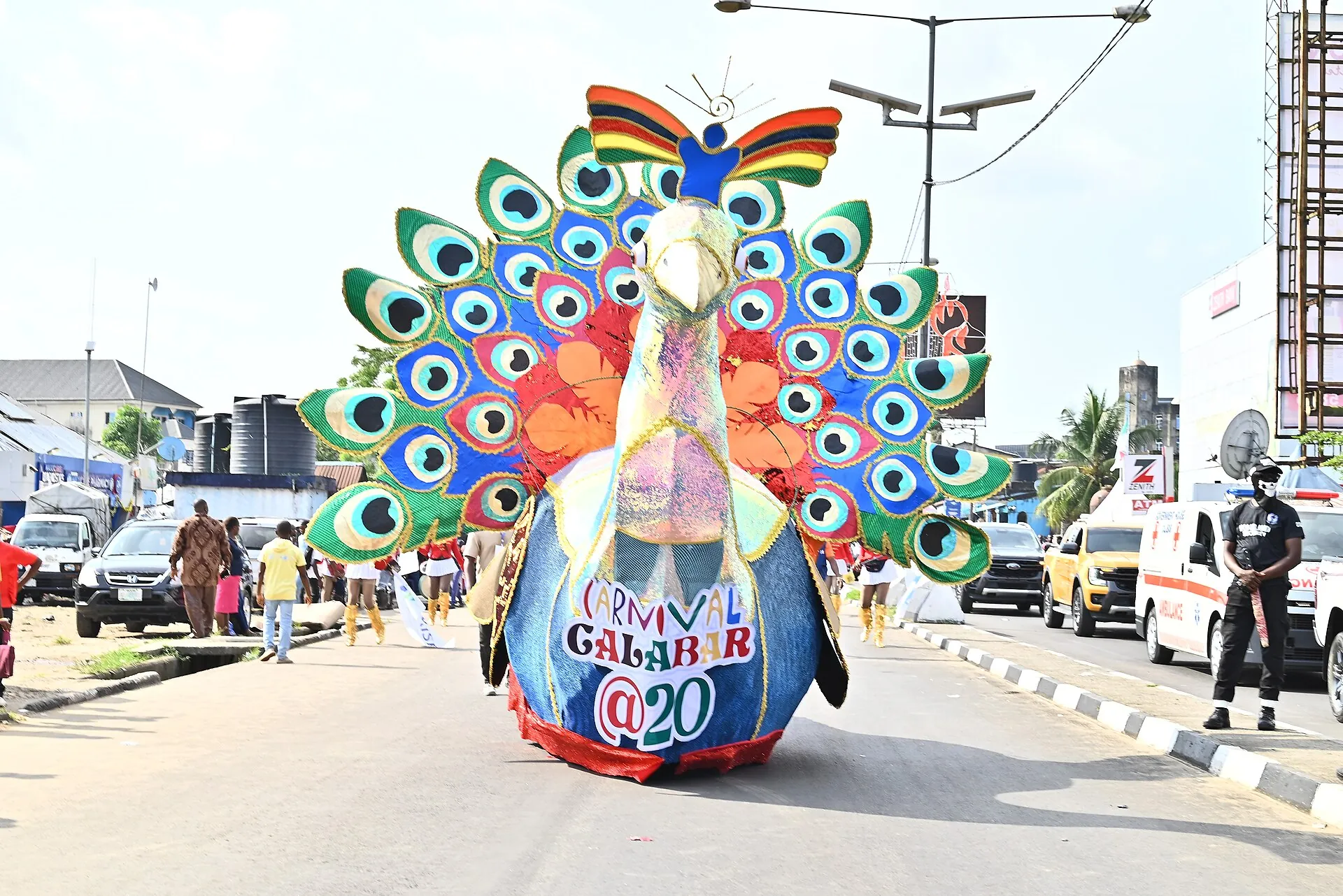 A Calabar Carnival costume shaped like a peacock, its fan of feathers in green, blue, and gold.