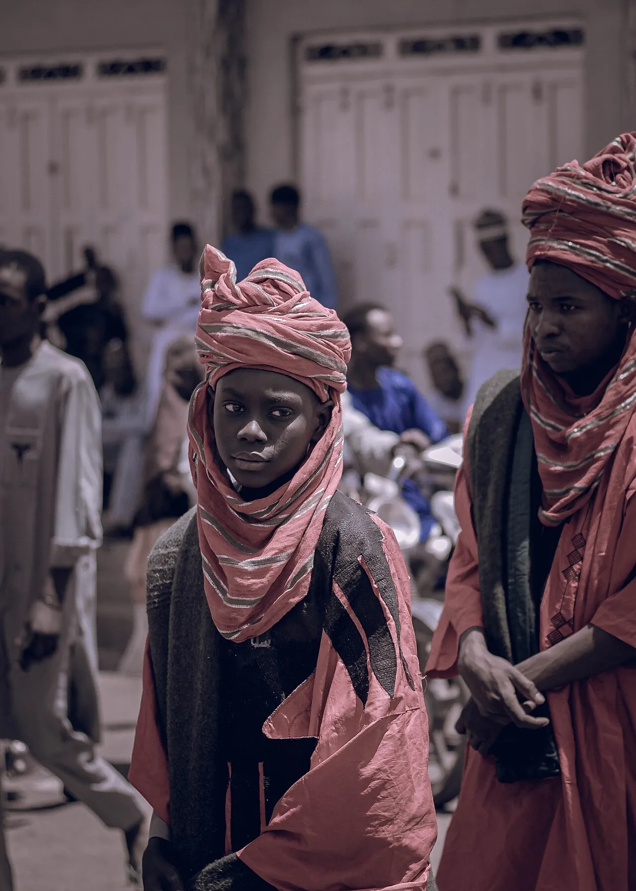 A rider at a northern Nigerian durbar in a pink turban and veil, with horsemen behind.