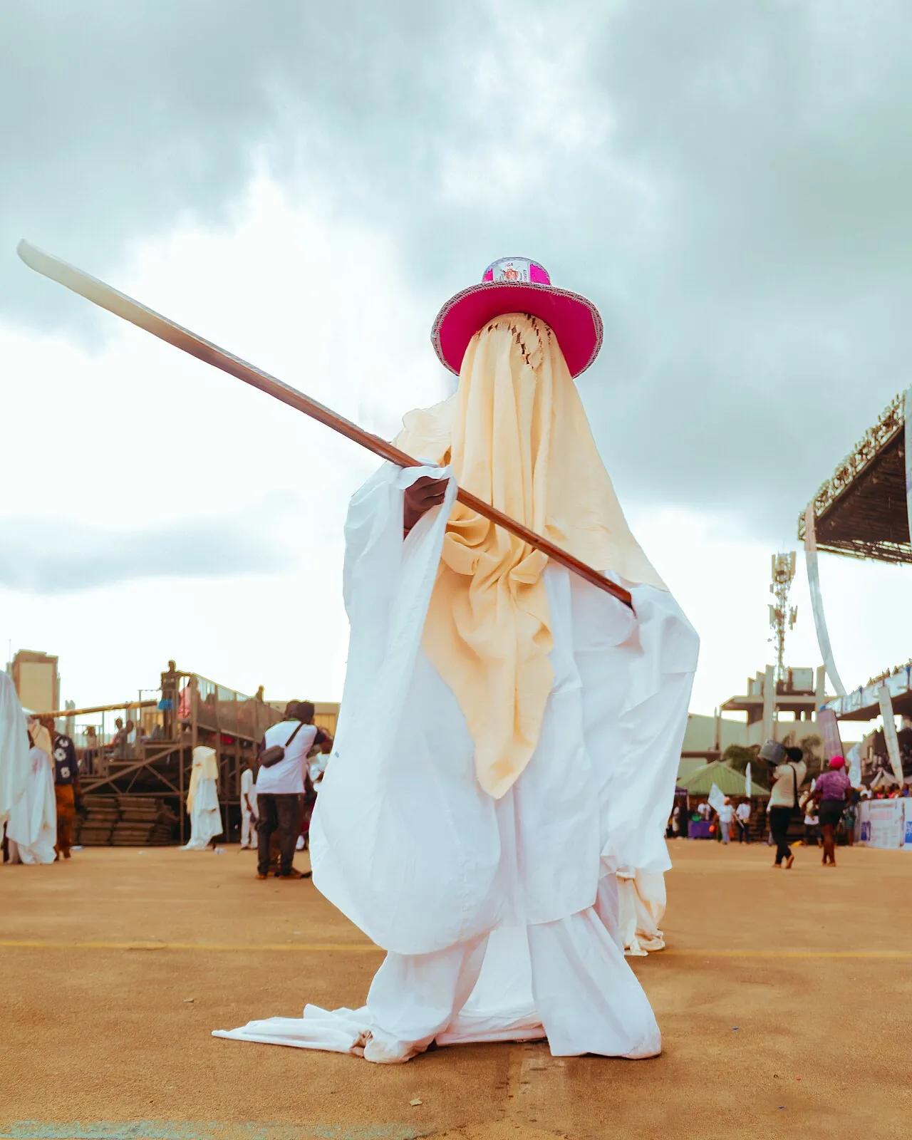 An Eyo masquerader in flowing white agbala and a red hat, staff raised, during the Eyo festival in Lagos.