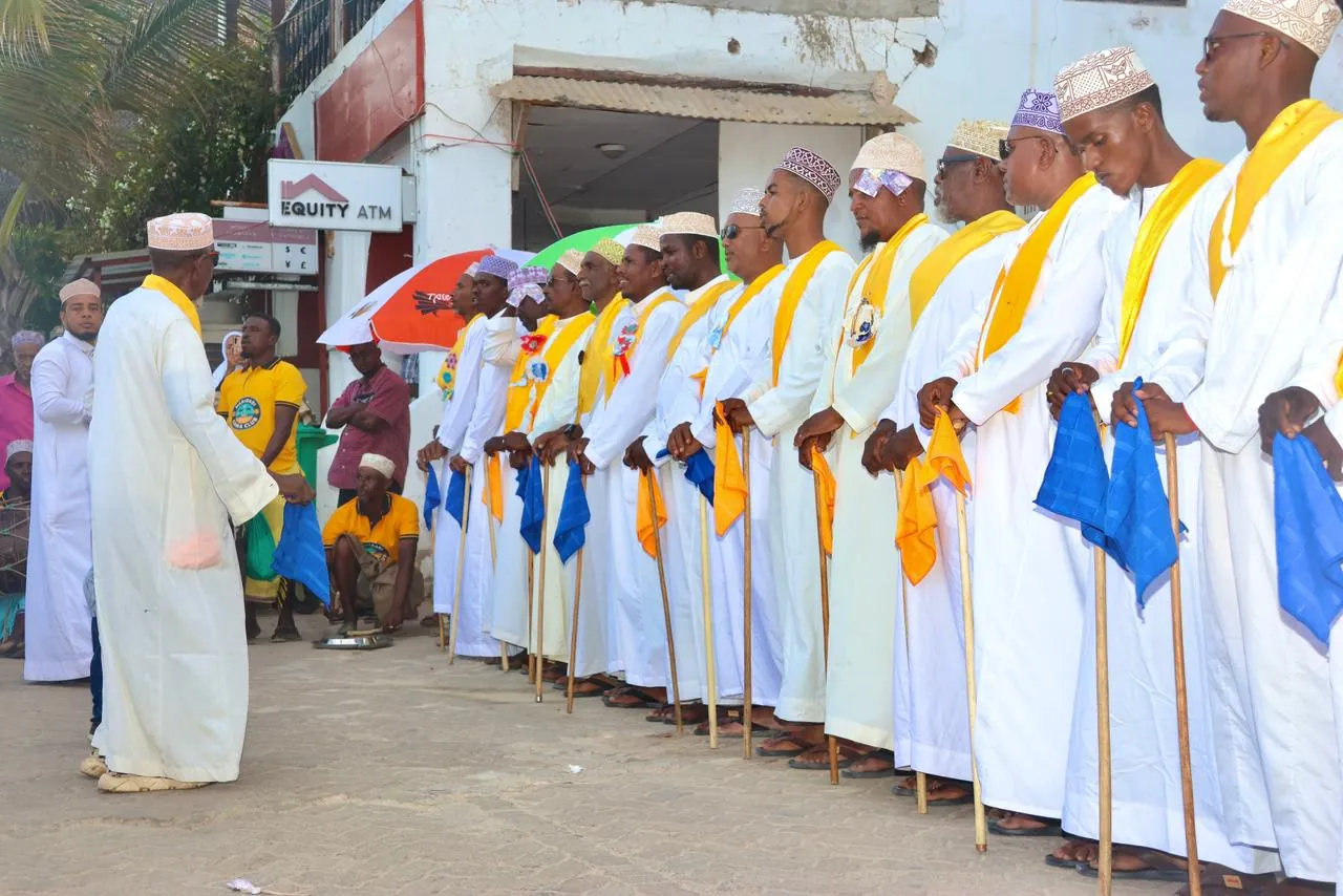 Men in white kanzu with yellow sashes, lined up at the Lamu Cultural Festival.