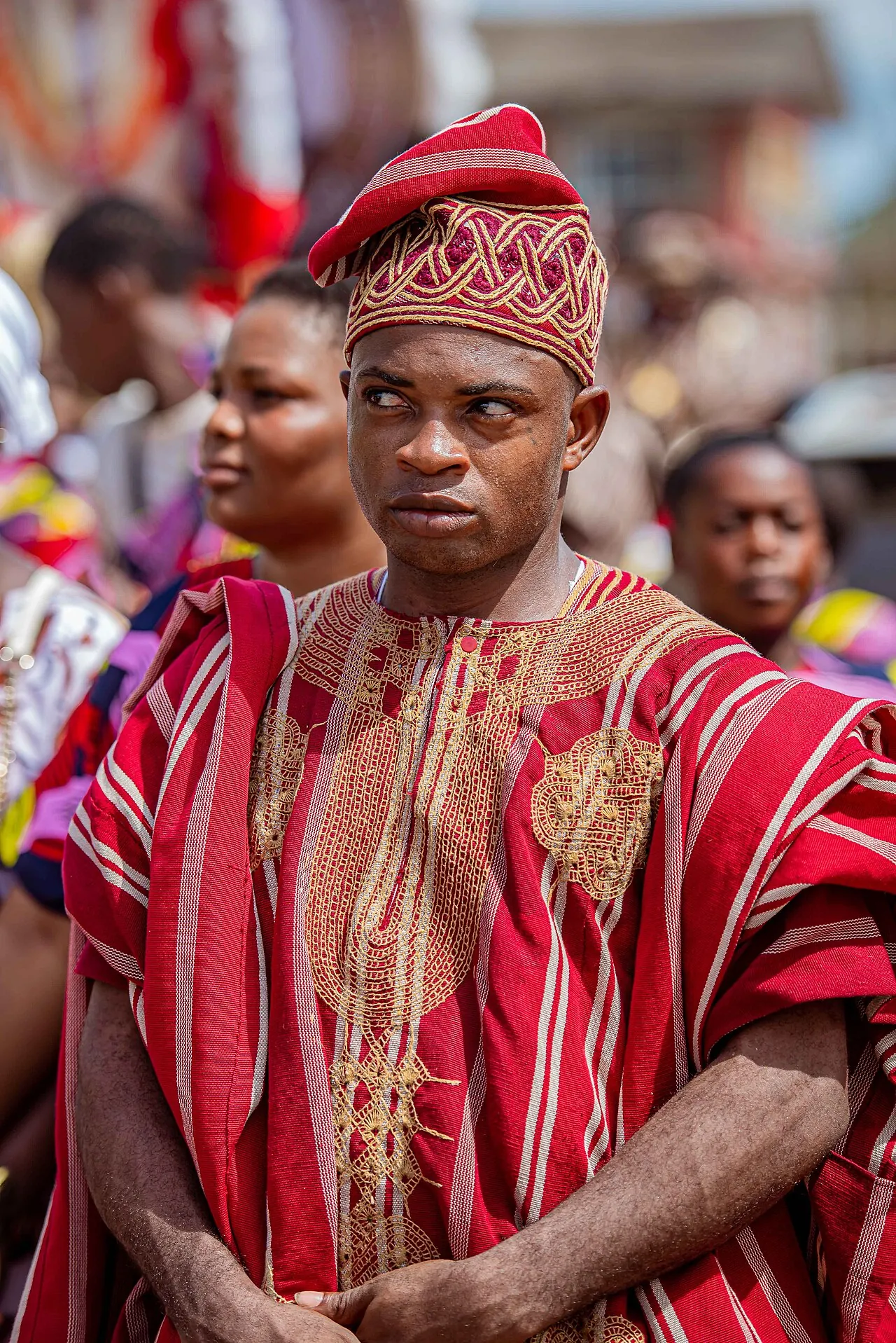A young man at Ojude Oba in red and gold aso-oke with a matching embroidered cap.
