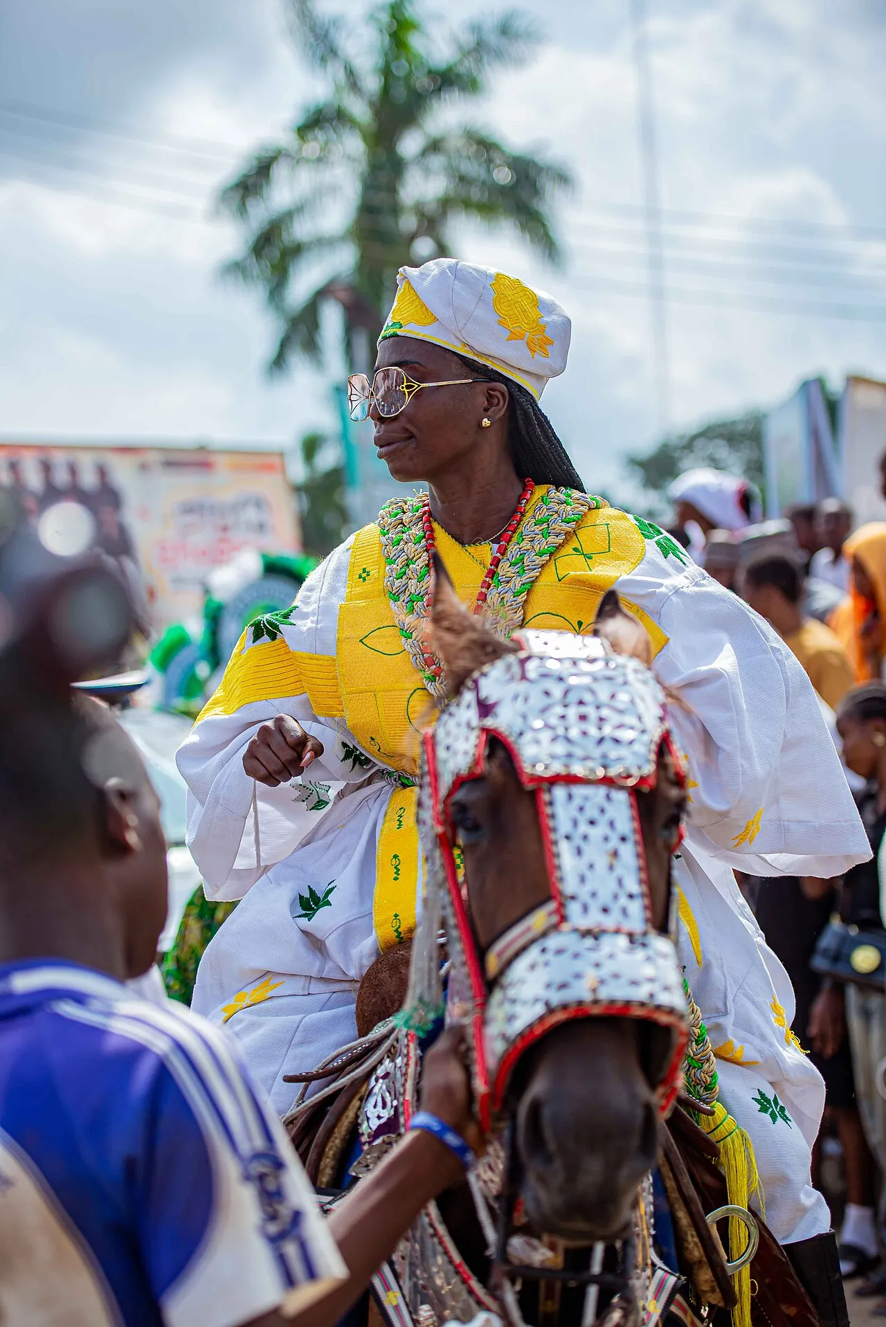 A rider at Ojude Oba in white and gold ceremonial dress and a gold headwrap, on a decorated horse.