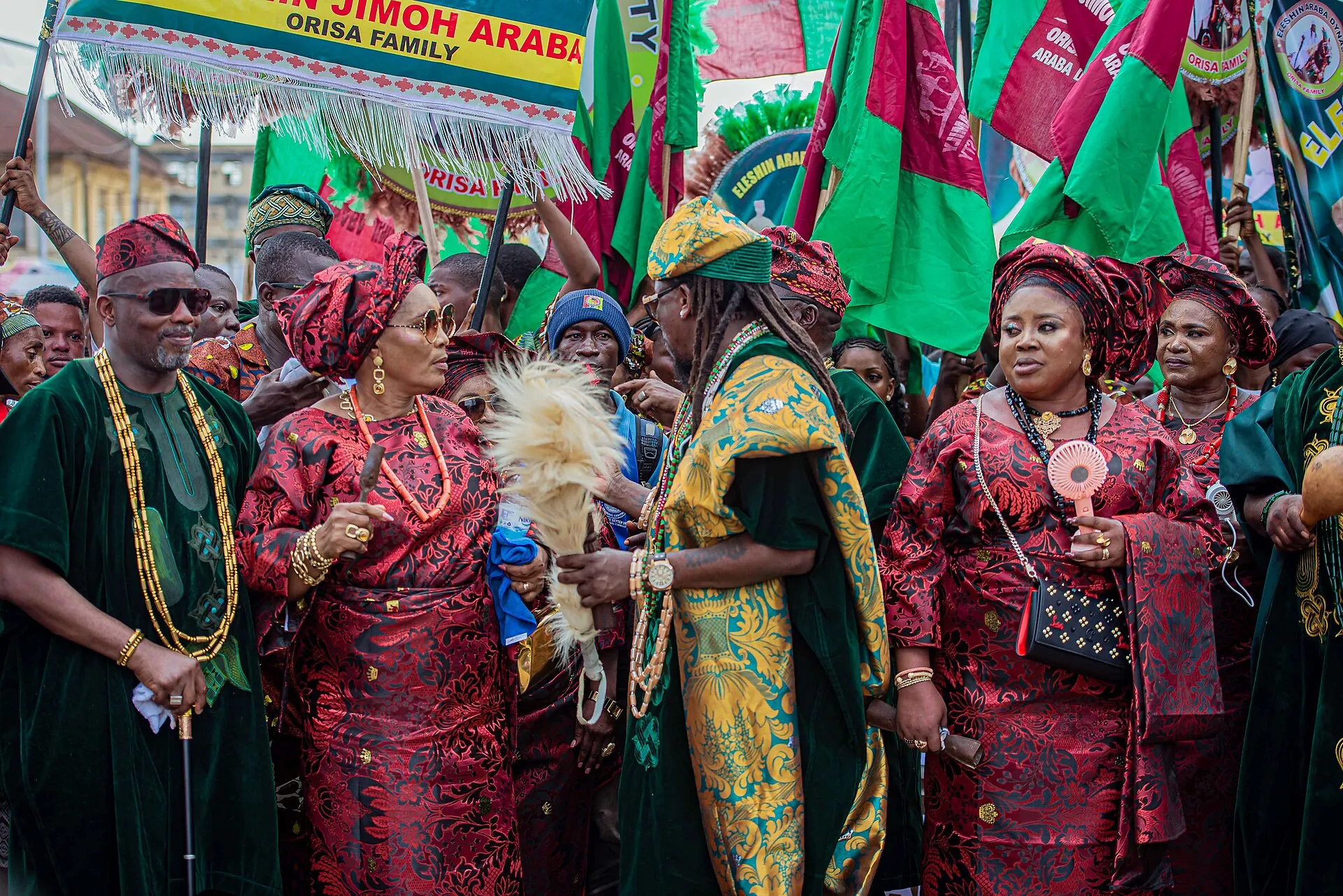 Women at Ojude Oba in matching red lace, coral beads, and gele, with chiefs in gold and green beside them.