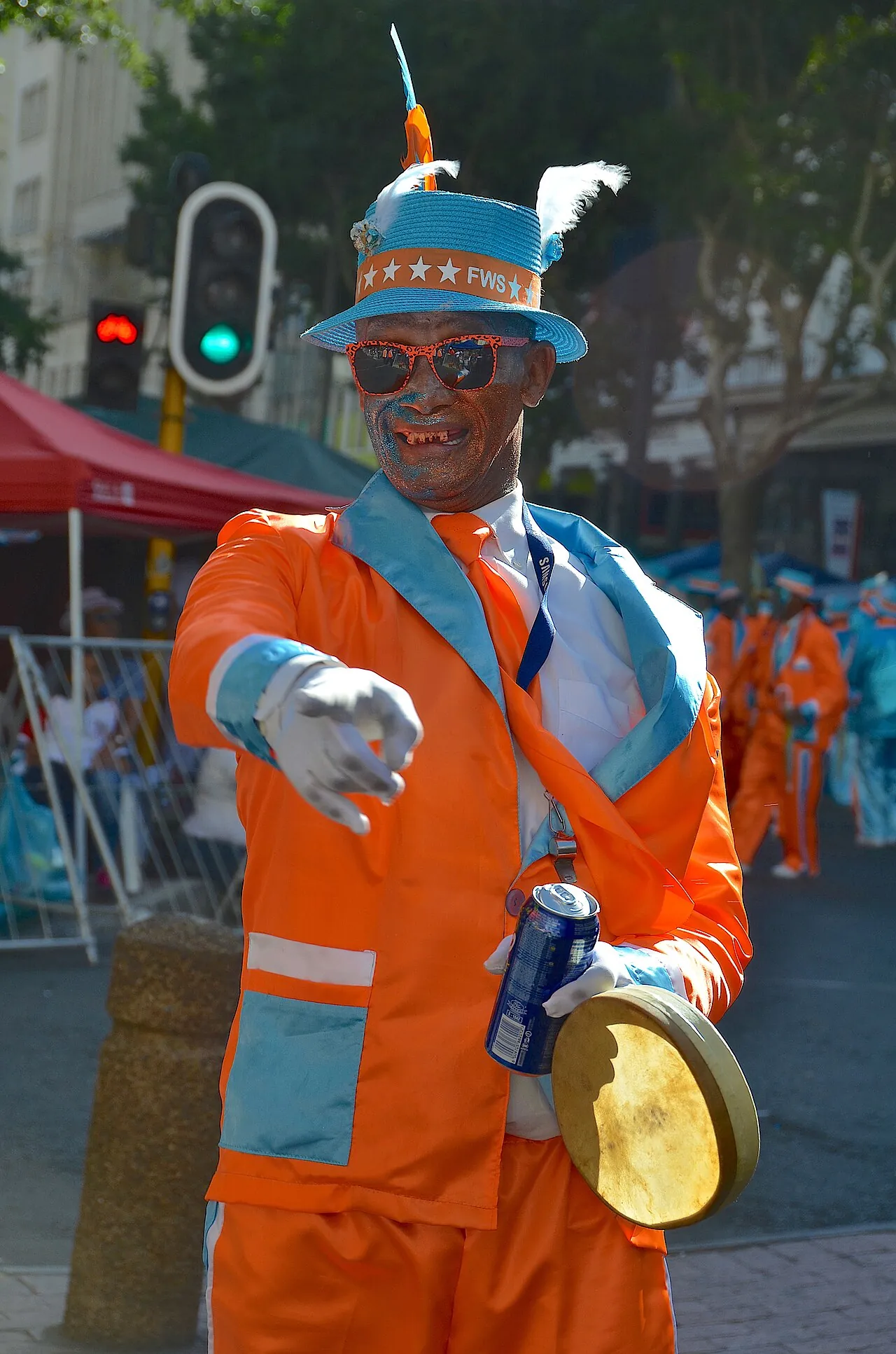 A Cape Minstrel in Cape Town in an orange and blue suit and a sequinned hat, holding a tambourine.