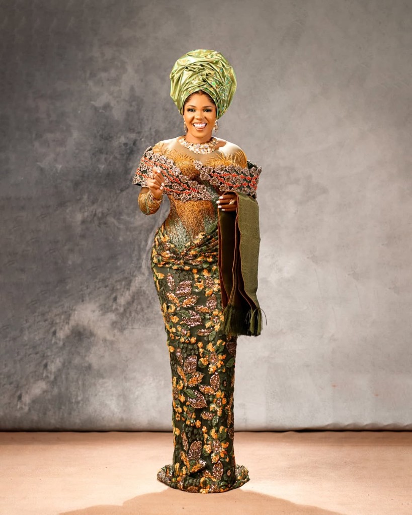 Iyabo Ojo in a green and gold gown with a matching gele, holding a fringed wrap.
