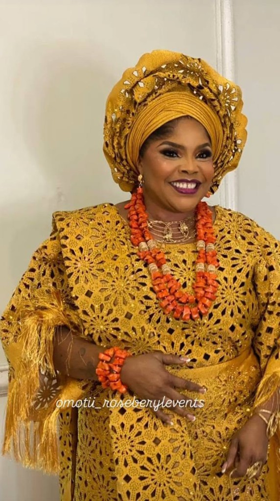 Lola Alao in a gold gele and a gold cutwork gown, with coral beads.