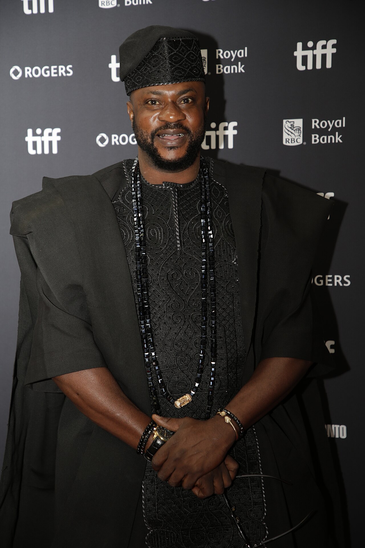Odunlade Adekola in a black agbada, embroidered fila, and long beads, at the Toronto International Film Festival.
